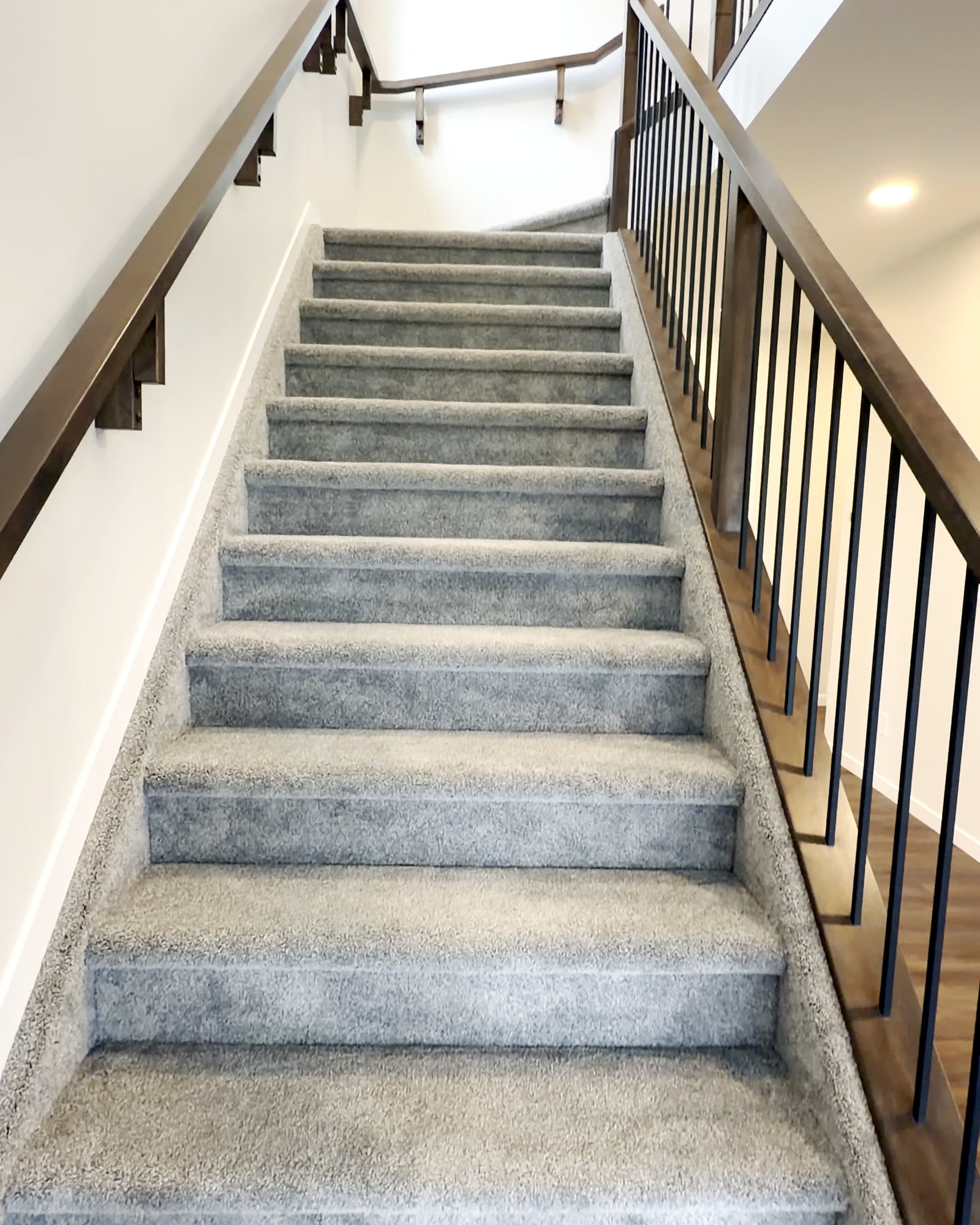 Carpeted staircase with wood railing and black spindles